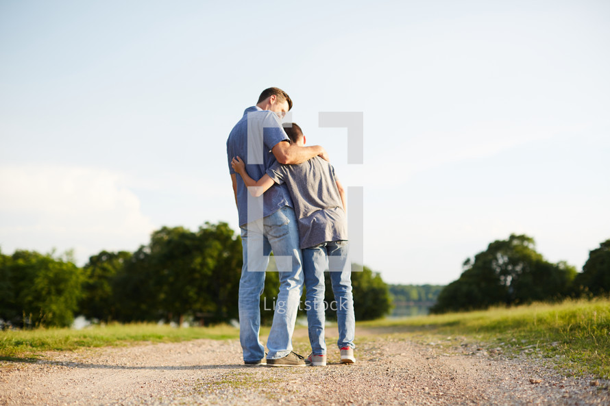 a father and son hugging standing on a dirt road 