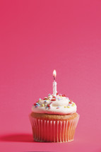 cupcake and candle against a fuchsia background 