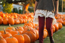a woman walking through a pumpkin patch 