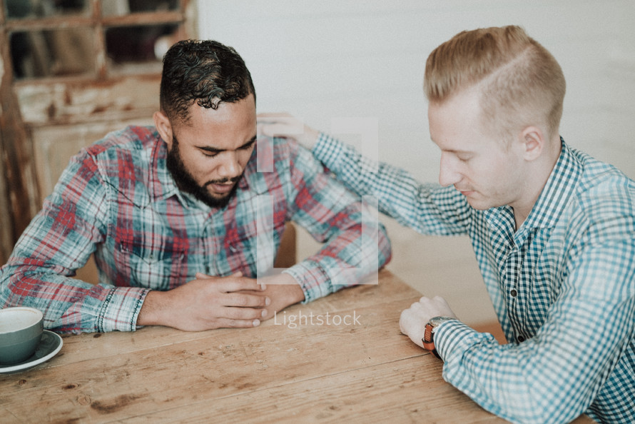 two men sitting at a table praying  
