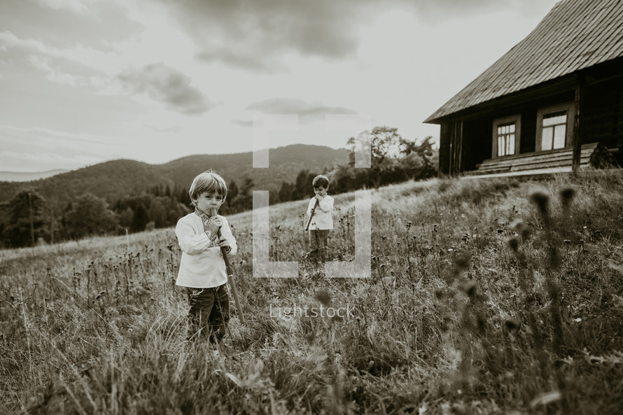 Little boys playing on woodwind wooden flutes - ukrainian sopilka on meadow of Carpathian mountain. Duet folk music concept. Kids in traditional embroidered shirts. High quality photo