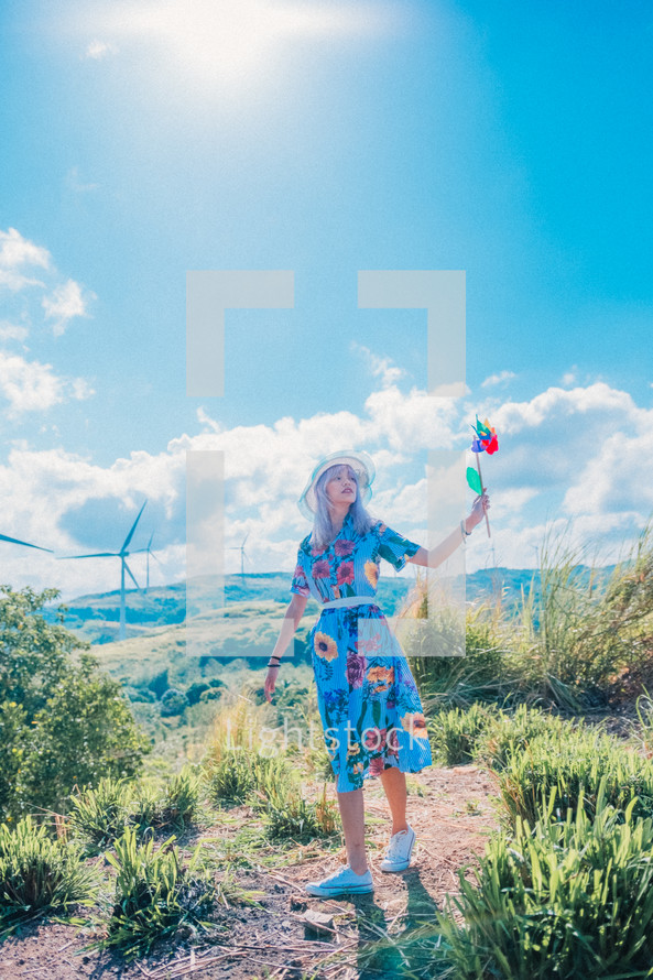 a woman holding pinwheels standing near wind turbines 