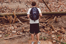 Teen with a backpack staring at debris.