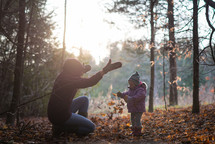 mother and toddler daughter playing in fall leaves 