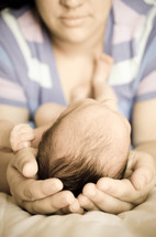 Mother cradling infant in her hands.