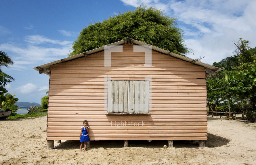 student in front of a small school house on a tropical island