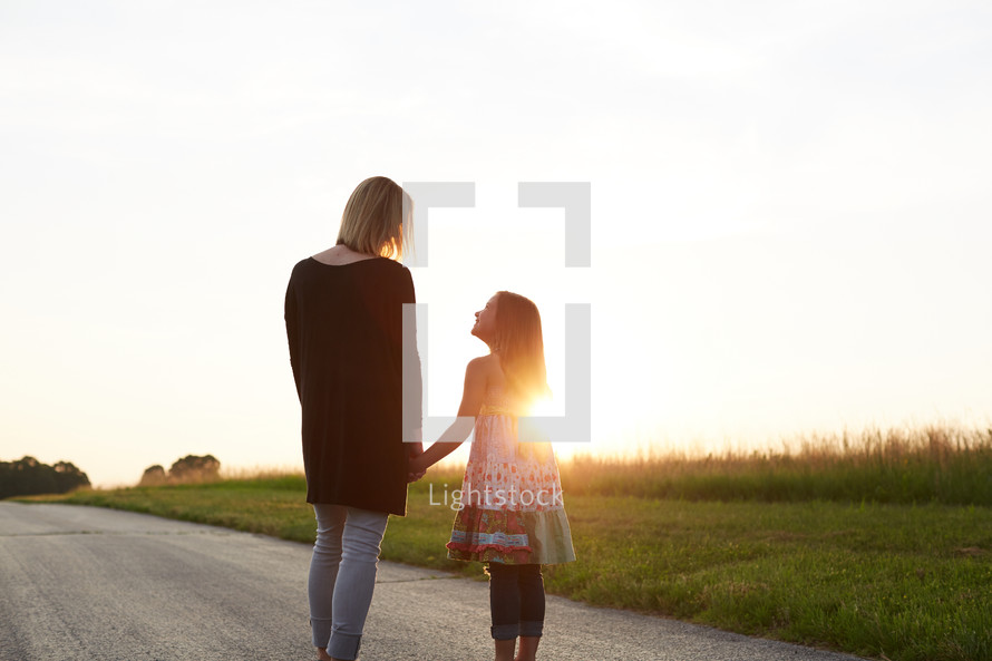 a mother and daughter standing together outdoors at sunset 