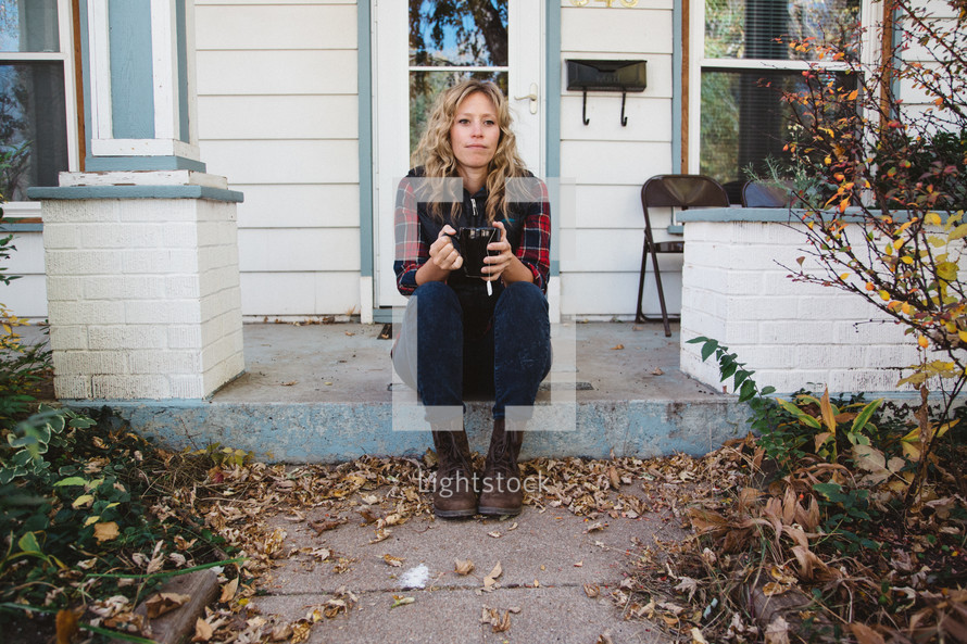 woman sitting on a stoop holding a mug of tea 