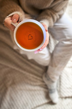 Woman holding mug of tea with heart in the bottom 