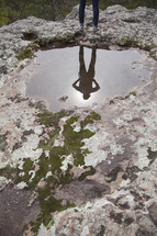 Person's reflection in a pool of water in a rock.