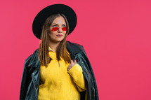 Pretty stylish woman on pink background. Smiling lady in hat and sunglasses with european appearance looking at camera. High quality photo