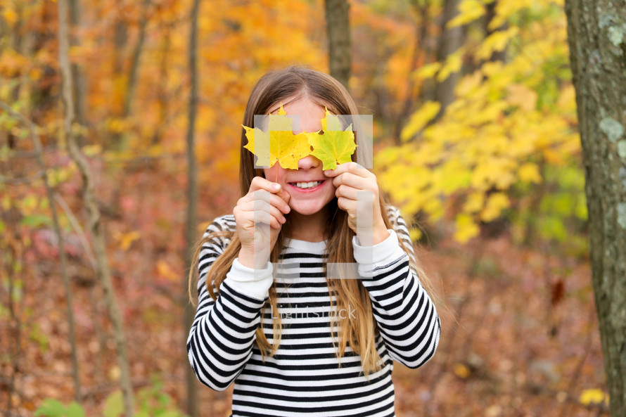 girl holding fall leaves in front of her face 