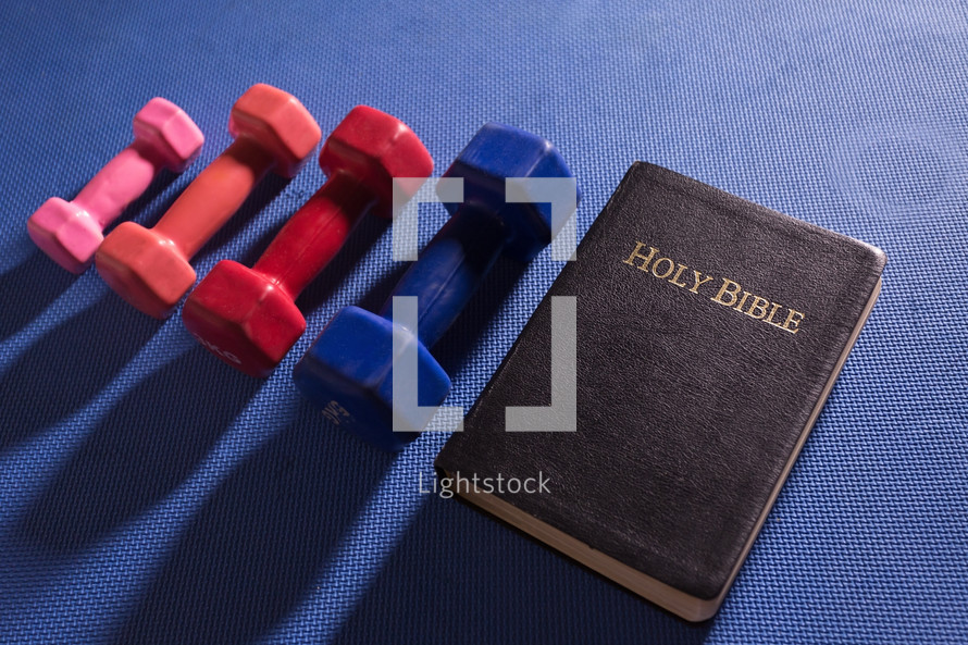 Dumbbells on a blue gym workout mat next to the Holy Scriptures