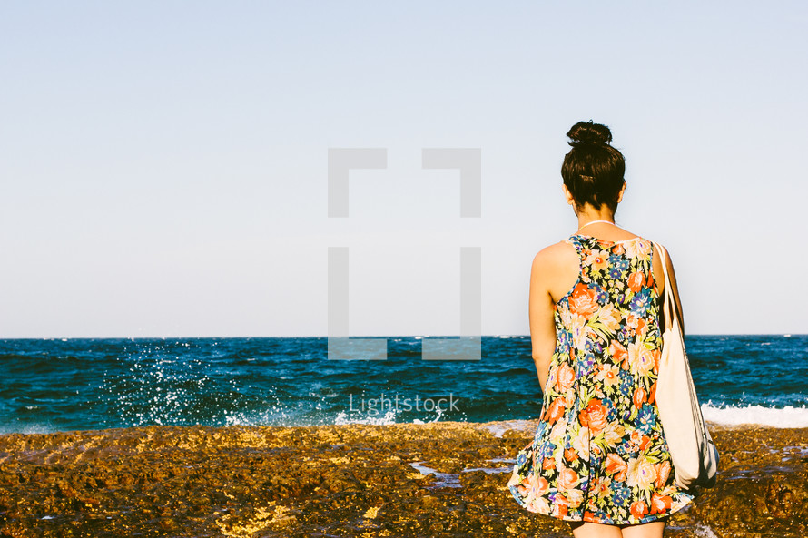 woman in a sundress standing on a beach 