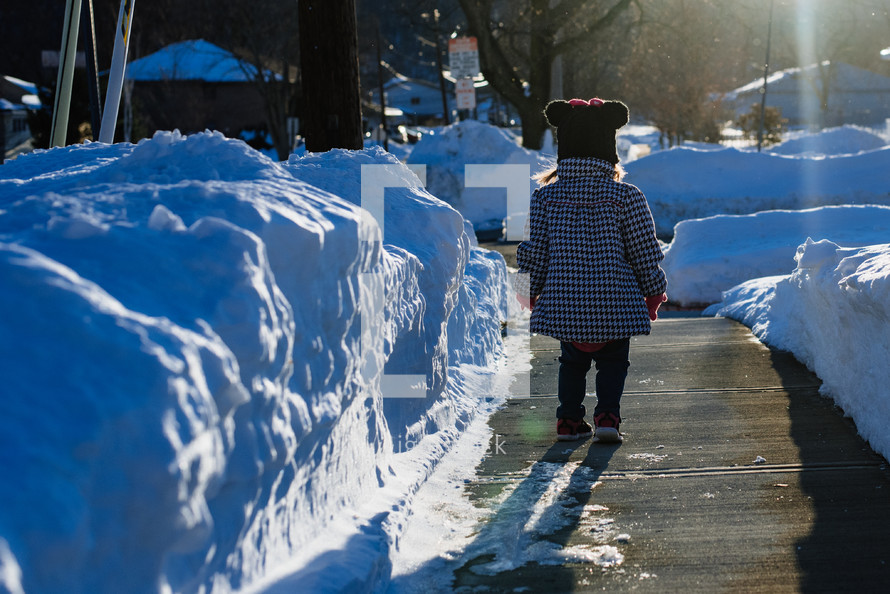 toddler girl on a plowed sidewalk in the snow 