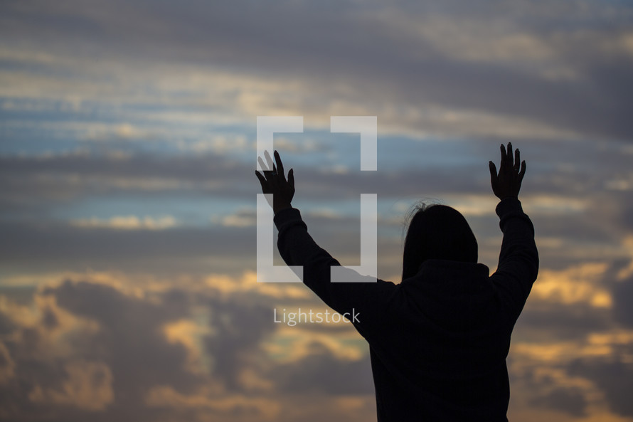 a woman with raised hands on at sunrise 