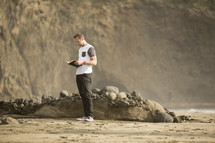 man standing on a beach reading a Bible 