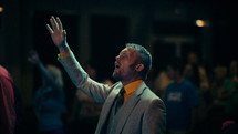 A man in suit and tie with hand raised in worship.