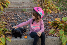 a child petting a black cat in fall 