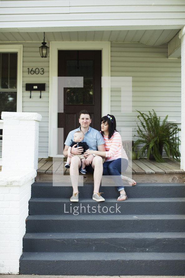 young family sitting on the front steps to their house 