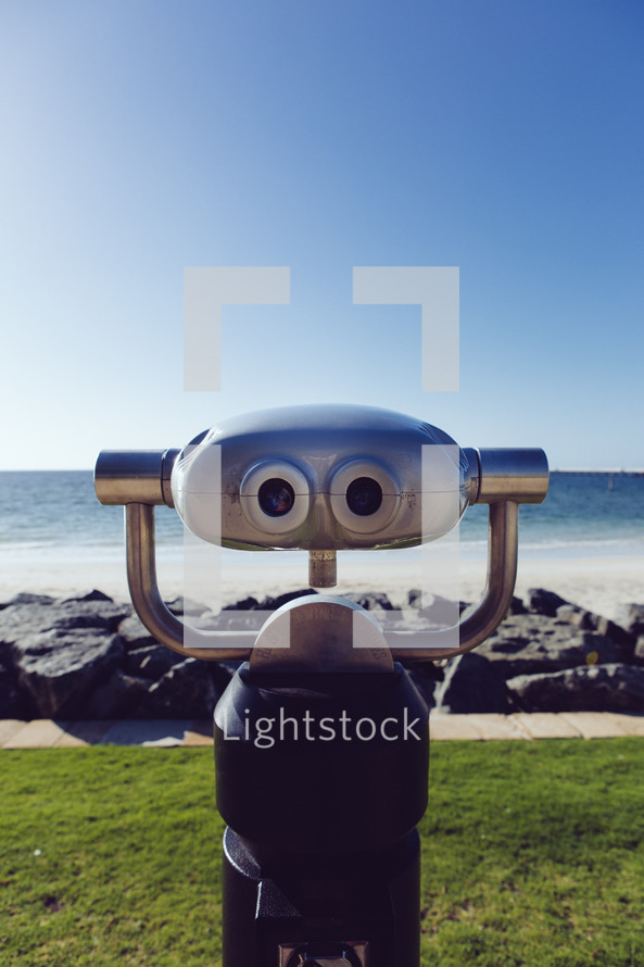 A robot stands in front of a rocky shore.