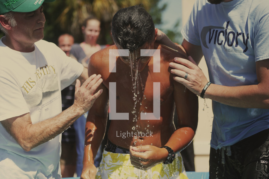 Two pastors lift a teen from a baptismal pool.