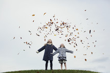 sisters tossing fall leaves in the air 