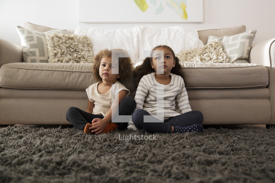 sisters sitting on a rug in a living room 