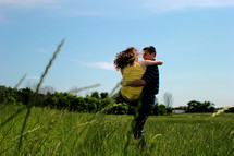 Man carrying a woman in a field of grass.