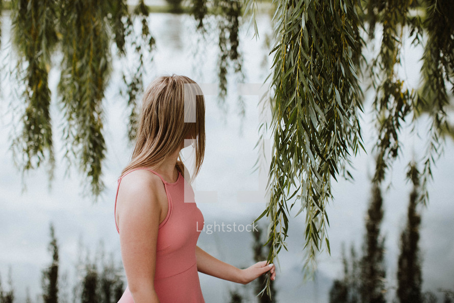 woman touching weeping willow branch by a pond 