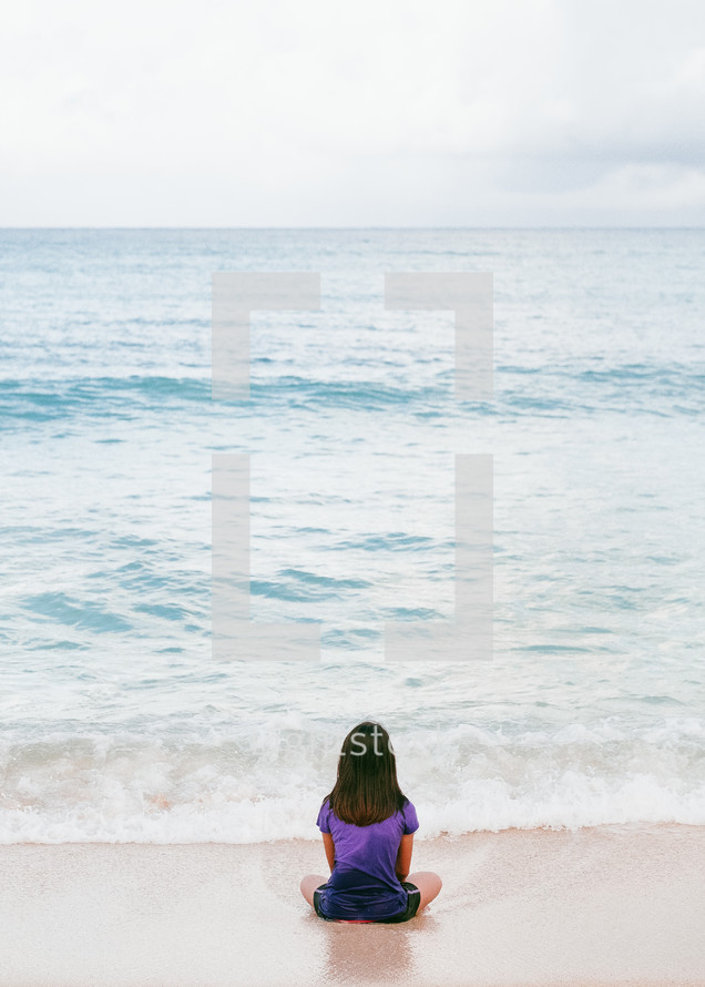 a girl sitting on a beach looking out at the ocean 