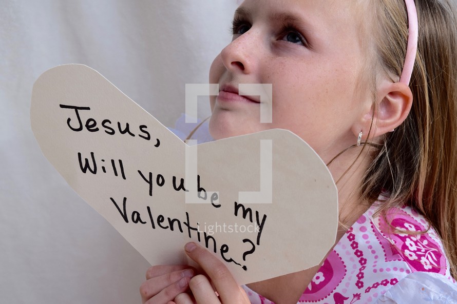 A little girl holding up a Valentine's day card for Jesus 