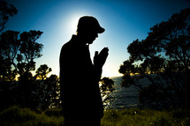 silhouette of a man in reverent prayer with praying hands 