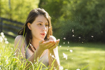 A young woman in a field blowing dandelion seeds.