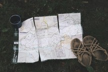 a trail map, sandals, and a coffee mug in grass 