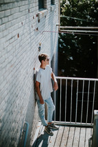 teen boy standing outdoors leaning against a white brick wall 