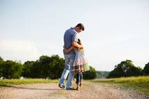 a father and daughter hugging on a dirt road 