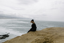 a woman sitting on the edge of a cliff by the sea 