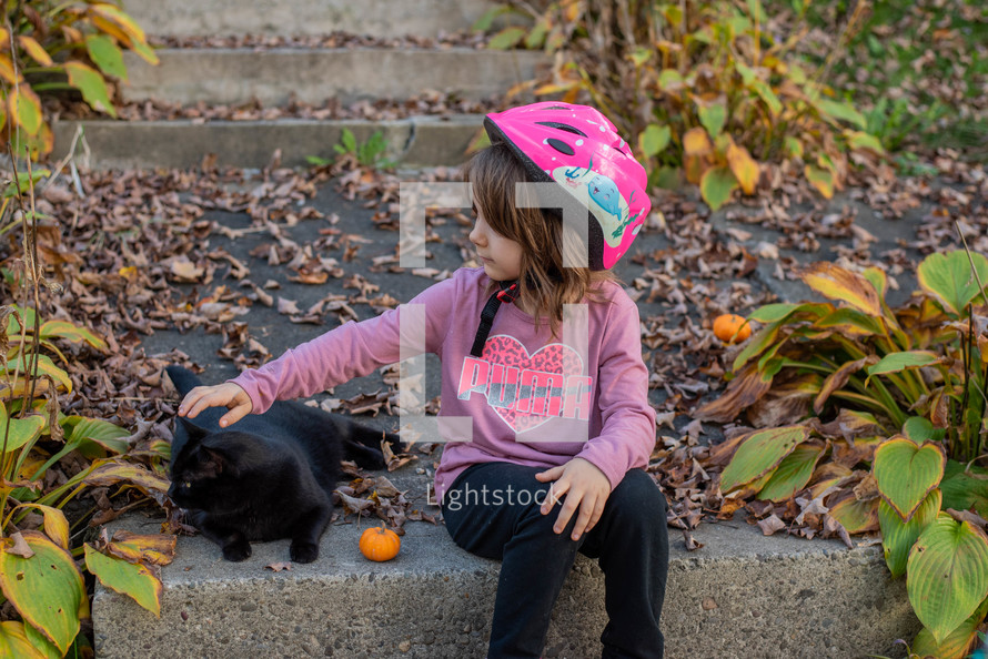 a child petting a black cat in fall 