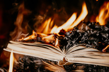 Old open book is burning. Big bright flame on papers. Destruction of diary in fireplace. Renunciation of past. Forbidden literature on bonfire. Censorship, prohibition of freedom information
