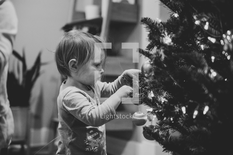 Small child hanging ornaments on a Christmas tree - black and white