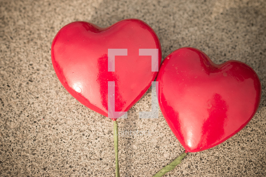 Two red hearts on sticks laying on a textured background