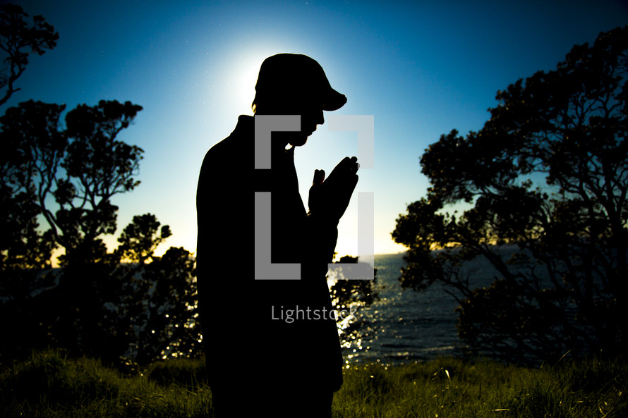 silhouette of a man in reverent prayer with praying hands 