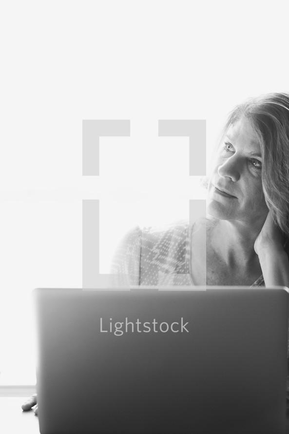 Woman in thought working at a laptop computer in the morning sun.