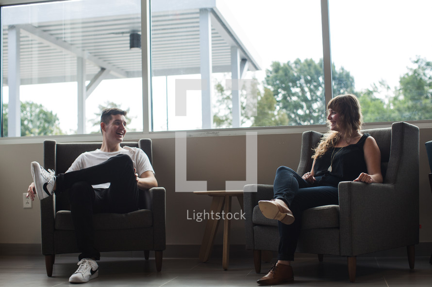 man and woman sitting in armchairs in a waiting area talking 