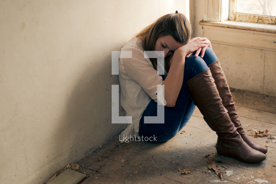 teen girl sitting alone in an empty room near a window 