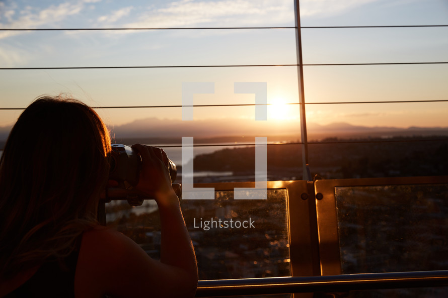 woman with a camera taking a picture from a balcony at sunset