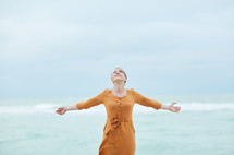 a woman standing on a beach with outstretched arms 