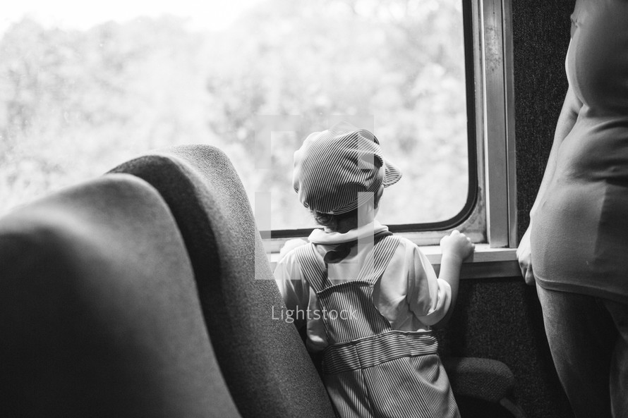 child in a conductor hat looking out a train window 