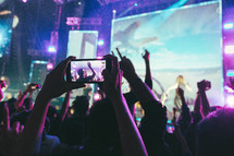 people in an audience at a concert  taking pictures of the stage with cellphones 